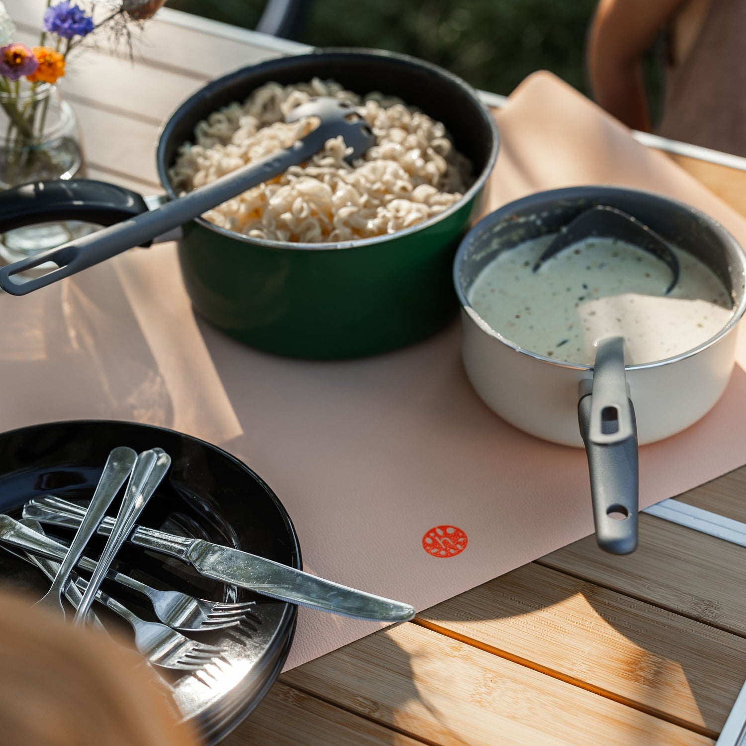 Wriggle Peach/Green silicone changing mat and placemat, camping dinner laid out on the mat with pots and wildflowers