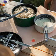 Wriggle Peach/Green silicone changing mat and placemat, camping dinner laid out on the mat with pots and wildflowers