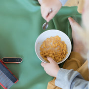 Wriggle Peach/Green silicone changing mat and placemat, child eating sweetcorn from a bowl on the sage green face