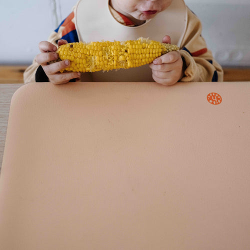 Wriggle Peach/Green silicone changing mat and placemat, toddler eating corn on the cob with the whole mat in view