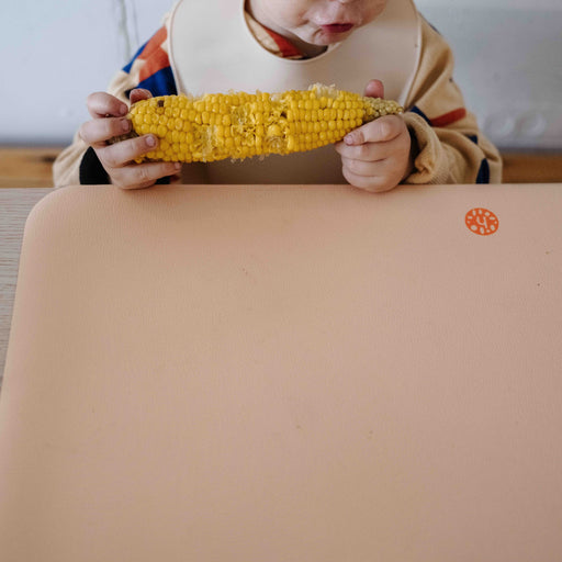 Wriggle Peach/Green silicone changing mat and placemat, toddler eating corn on the cob with the whole mat in view