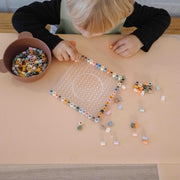 Wriggle Tapis à langer et set de table en silicone pêche/vert, un tout-petit enfile des perles à repasser à sa table