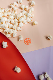 Vegan leather play mat with round design, featuring scattered popcorn and colorful surface.