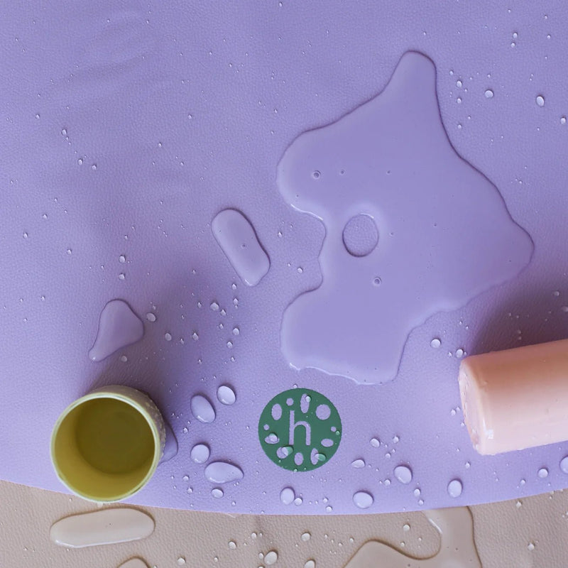 Vegan leather play mat showing a purple surface with water droplets and small play items.