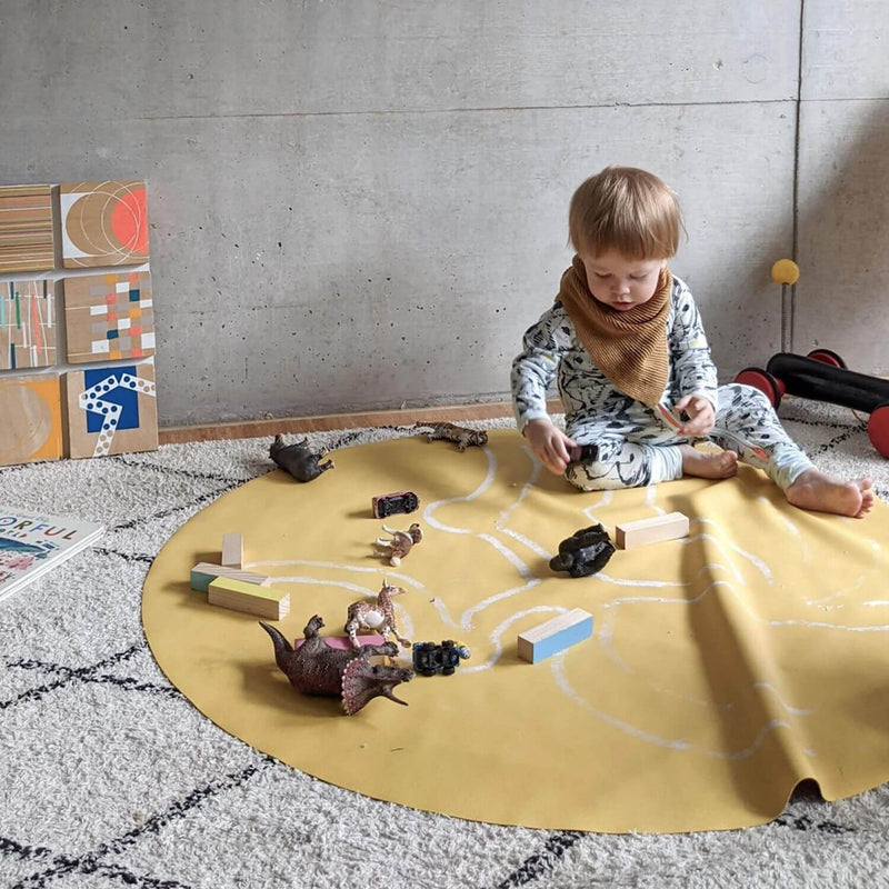 Child playing on a silicone leather play mat surrounded by toys and blocks in a modern indoor setting.