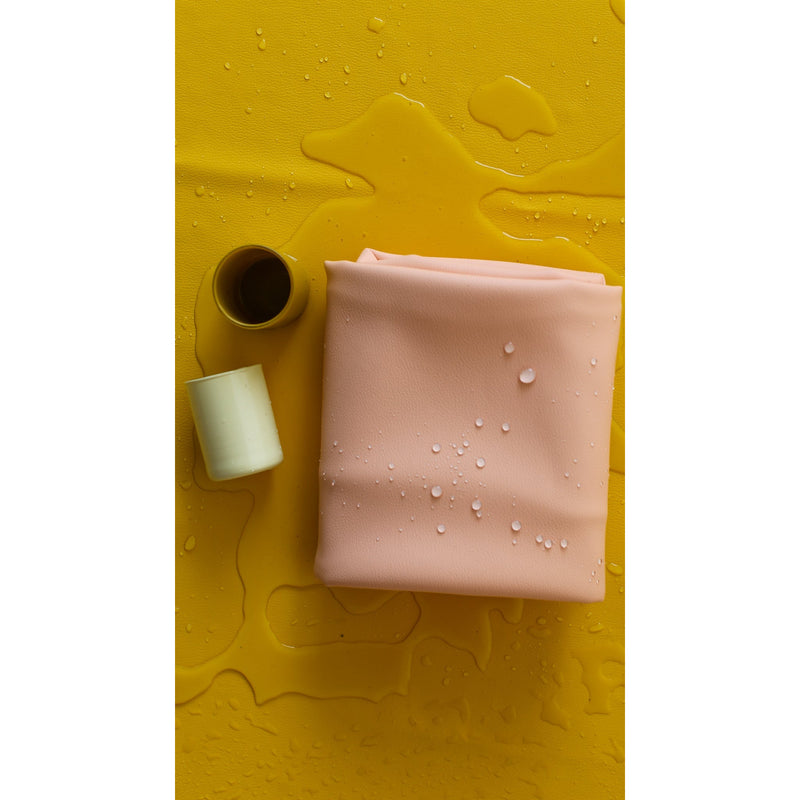 Vegan leather play mat in peach color with water droplets on yellow background, ideal for play activities.
