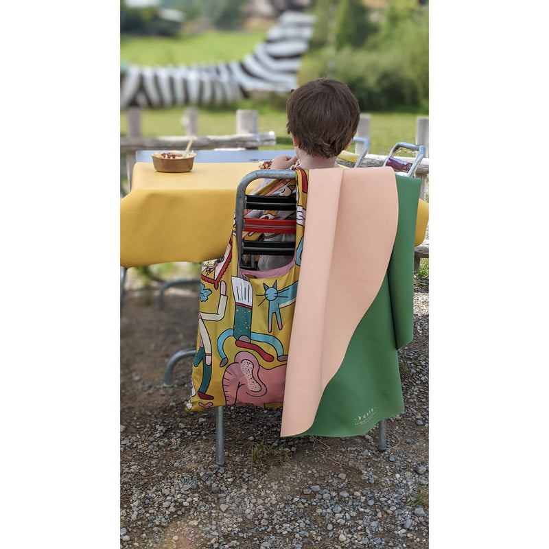 Child sitting at a table outdoors with a vegan leather play mat draped over a chair, enjoying a meal.