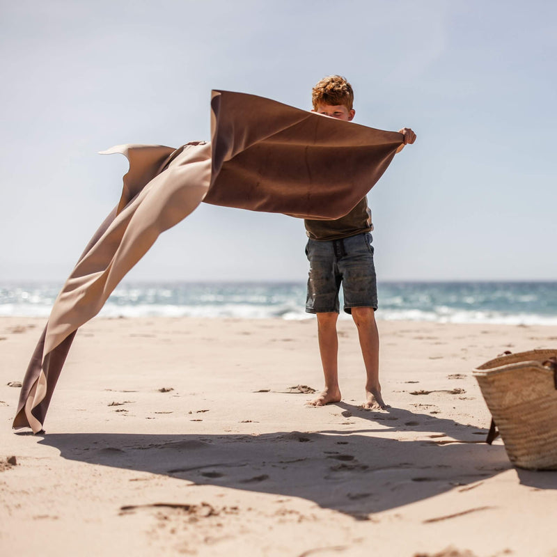 Boy holding an extra large waterproof silicone mat on the beach, showcasing its spacious design for family fun.