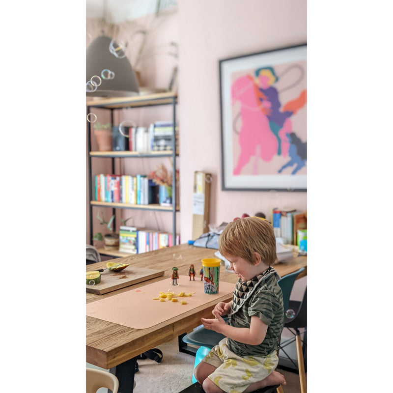 A child playing on a waterproof silicone leather changing mat, Wriggle Mat (S), featuring toys and a cozy home setting.