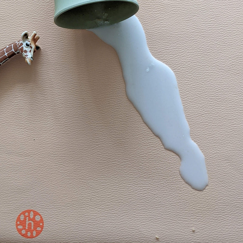 Waterproof silicone leather changing mat with spilled milk and a toy giraffe beside it.