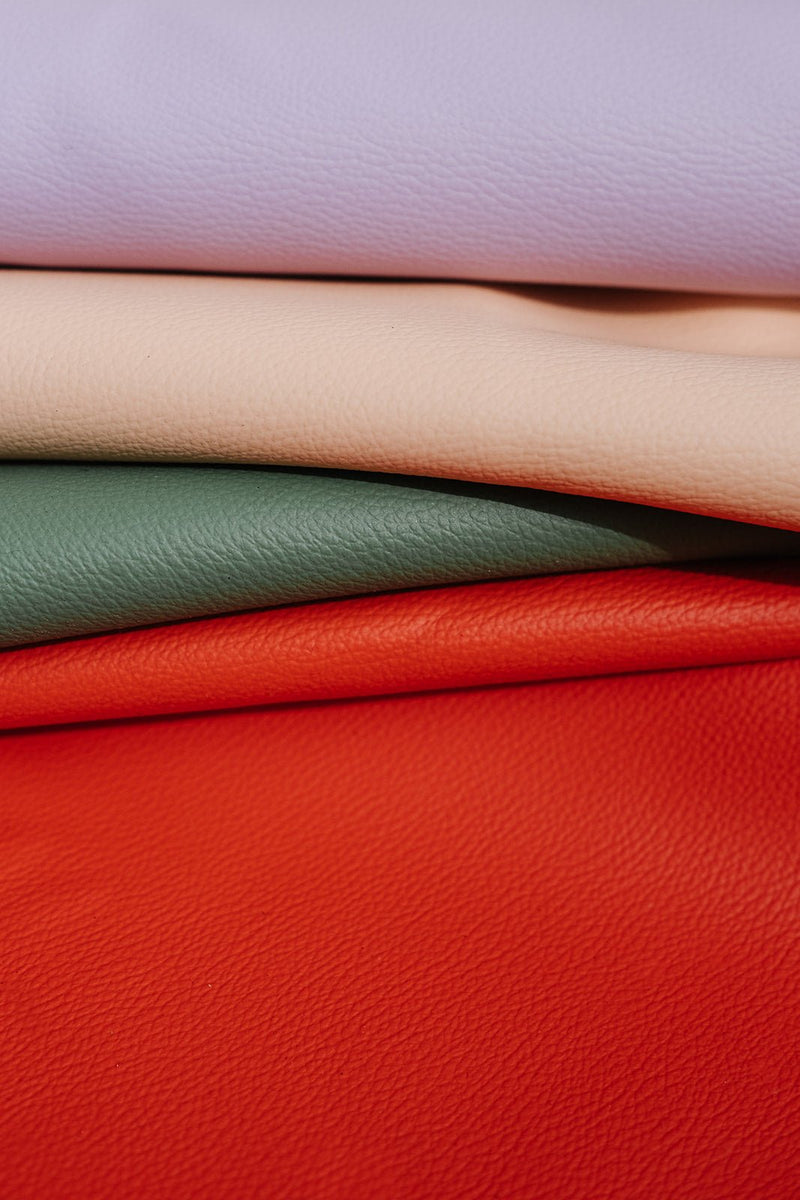 A stack of colorful premium faux leather materials in lilac, beige, green, and orange for design and craft projects.