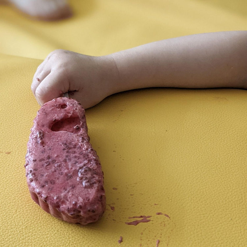 Child's hand holding colorful play dough on a waterproof silicone leather changing mat.