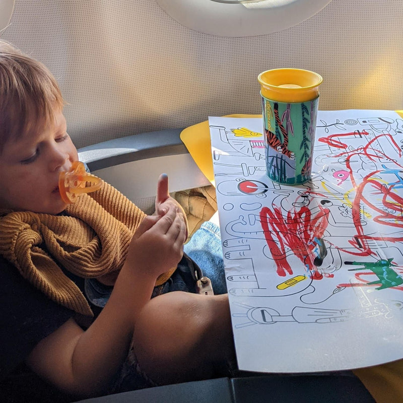 Child using a waterproof silicone leather changing mat for play, colored drawings, and a sippy cup on an airplane.