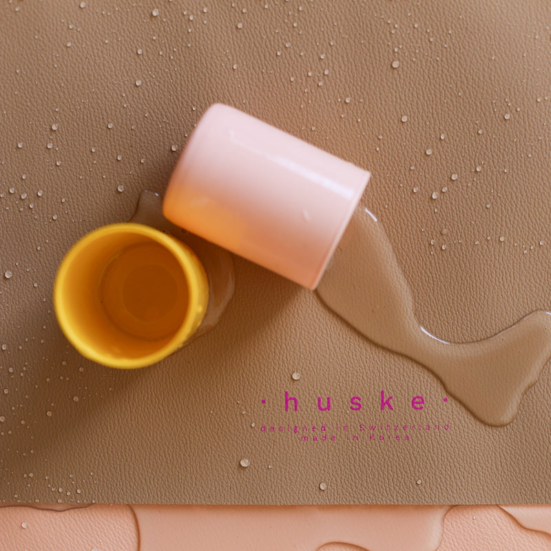 Waterproof silicone leather changing mat with spills from yellow and pink cups.