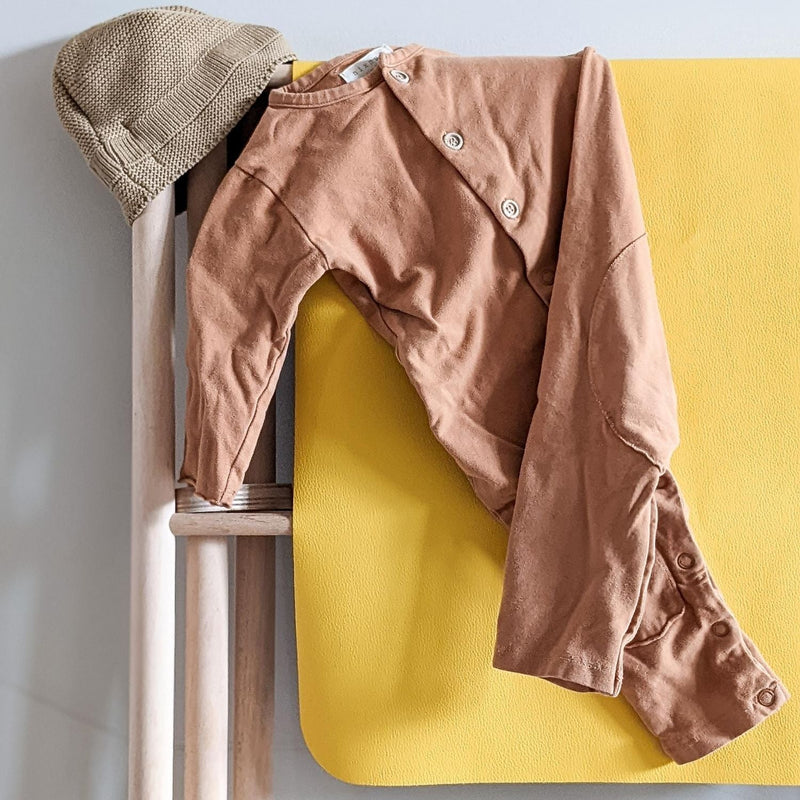 Stylish brown long-sleeve outfit with buttons and a knit hat on a bright yellow changing mat.