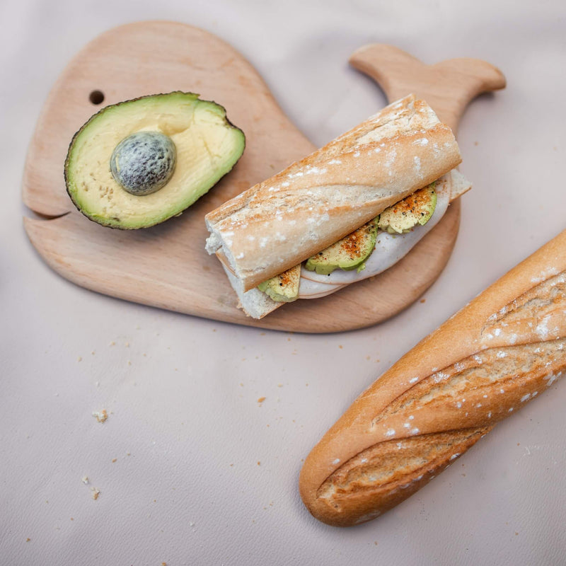 extra large waterproof silicone mat with sandwich and avocado resting on a whale-shaped wooden platter.